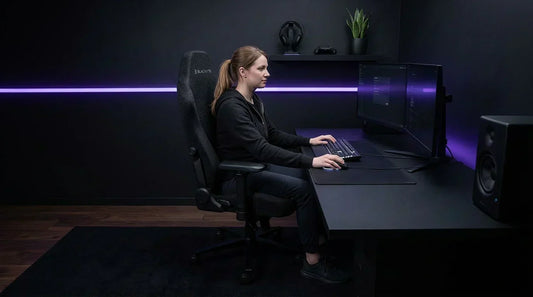 Gamer at an all-black stealth battlestation in an ergonomic matte black gaming chair — long session lumbar support setup